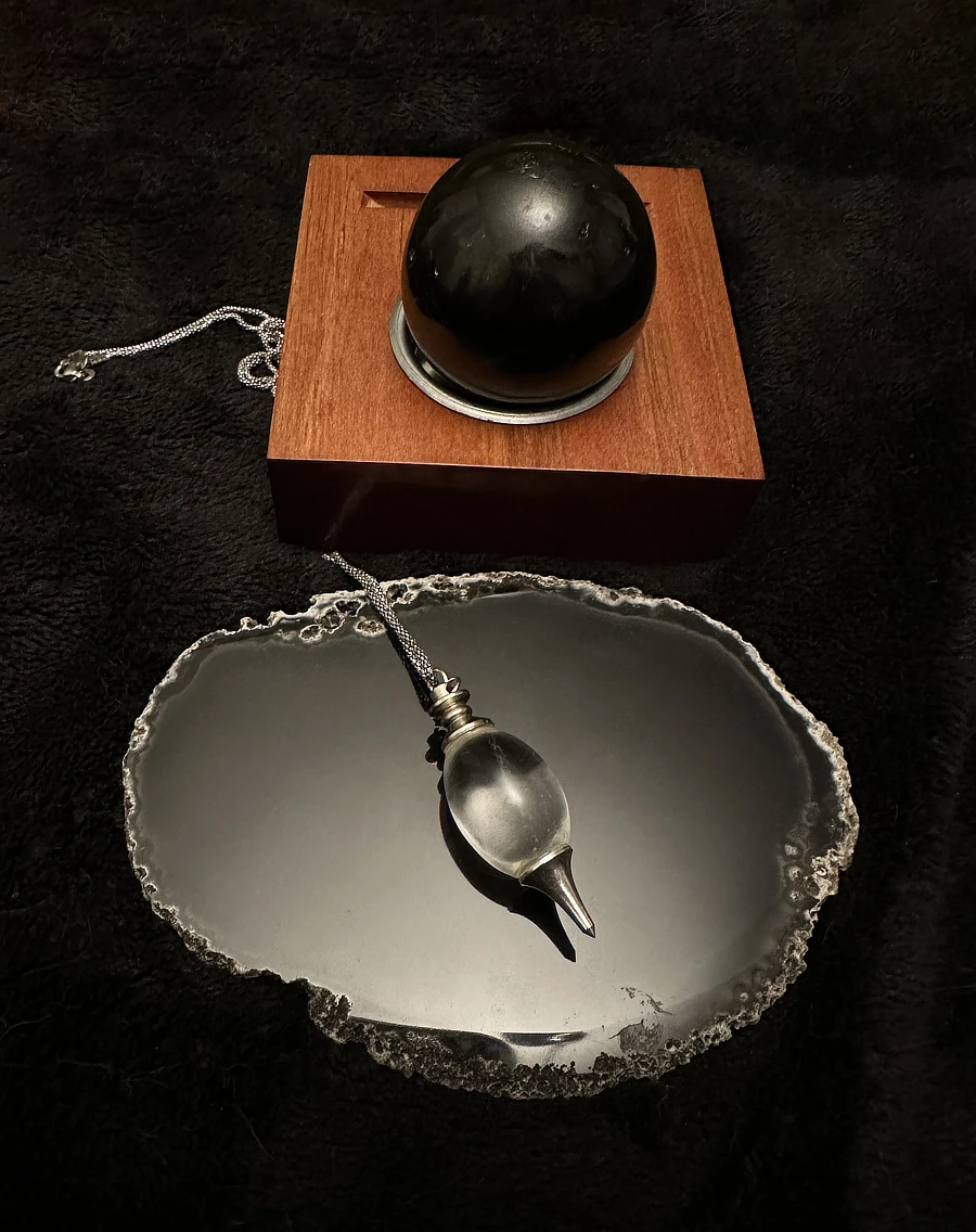 Strumenti del collettivo Black Mirror Academy per i consulti: una sfera di tormalina nera, una lastra di agata oscura e un pendolino di cristallo